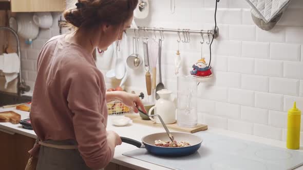 Woman frying mushrooms and onions in pan on stove