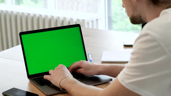 Over the shoulder businessman at home office sits table, communicates talk speak with green screen