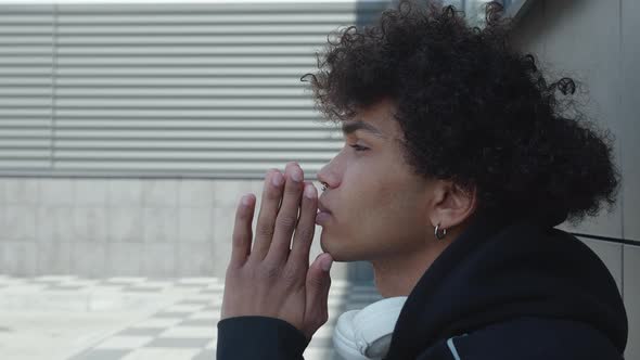 A Young Afro American Guy in a Black Hoodie Sitting Near a Concrete Wall Praying or Very Thoughtful