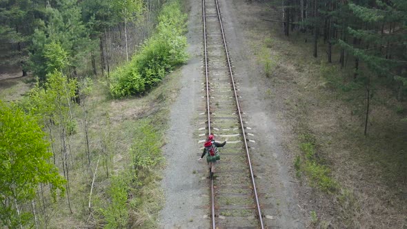 Tourist with a Backpack Goes on the Rail of the Railway. Balances and Tries Not To Fall. Aerial View