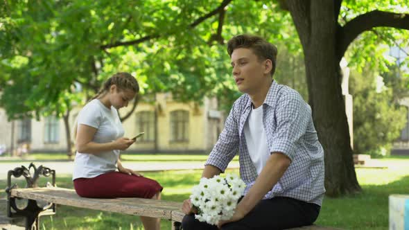 Nervous Teenager Presenting Flowers to Girl in Park