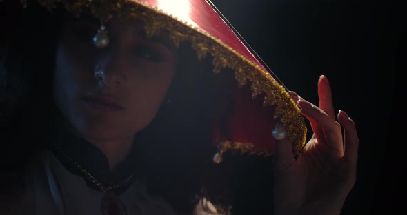 Portrait of a Young Beautiful Geisha in Red Hat Posing in a Dark Room, 
