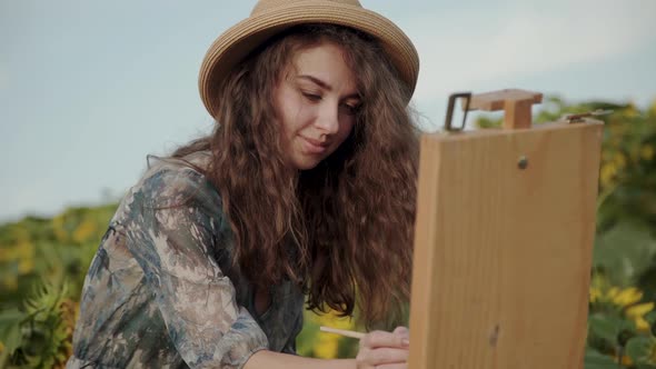 Cheerful Longhaired Lady Painting Landscape with Watercolors Among Sunflowers