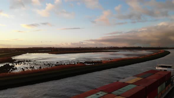 Fully loaded cargo vessel sailing with containers on the dutch river Noord while the sun gives the n