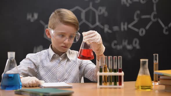 Schoolboy Looking at Red Liquid in Flask and Scratching Head, Having No Idea