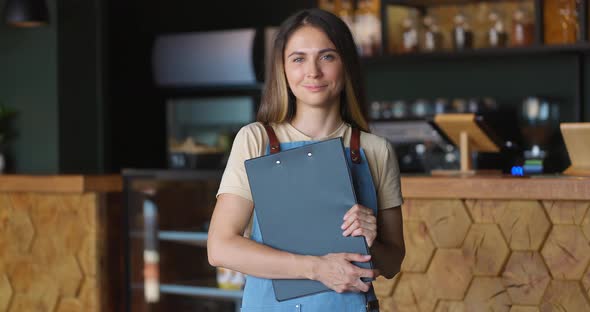 Portrait of the Beautiful Brunette Waitress in Apron with Tablet in Hands Smiling Cheerfully at