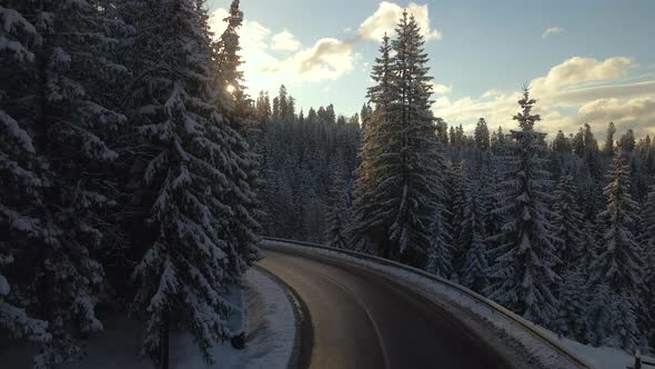 Aerial view of winter landscape with snow covered mountain hills and winding forest road in morning.