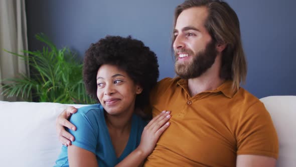 Mixed race couple embracing each other while sitting on the couch at home