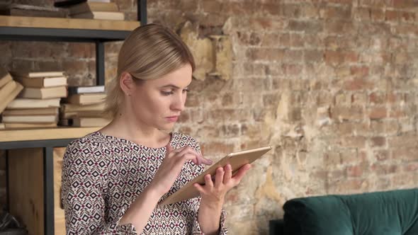 Good Looking Woman Using A Tablet near bookshelf. Beautiful girl touch computer