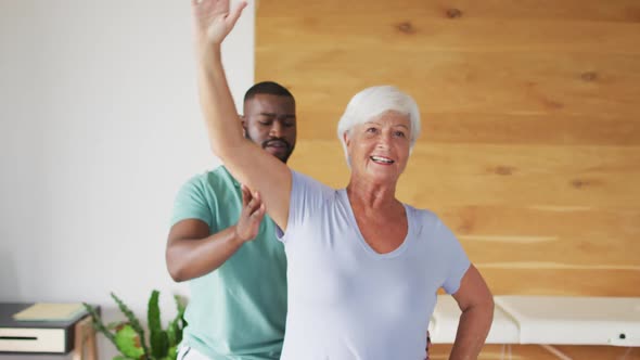 Video of happy african american male physiotherapist examining caucasian senior woman