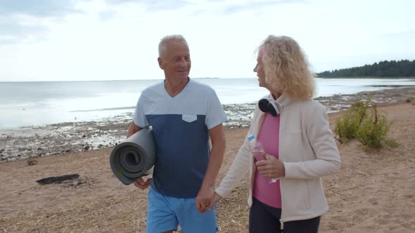 Senior Sporty Couple Holding Hands Walking on Empty Beach Relaxing After Workout