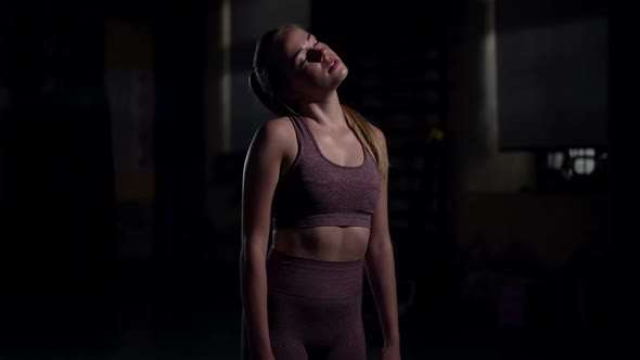 Young Sportswoman Warming Up Neck Muscles Stretching in Slow Motion Standing in Darkness