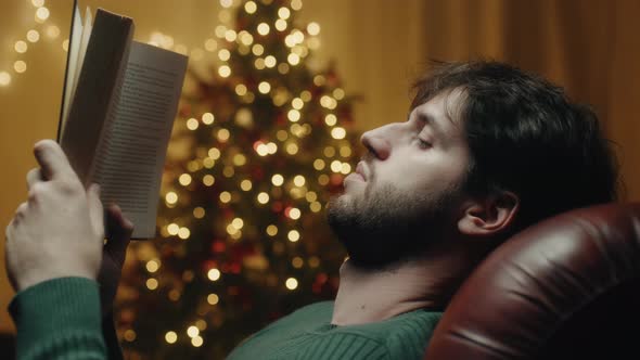 Boy reads book beside Christmas tree