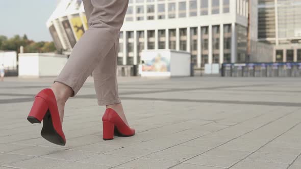 Business female legs in red high-heeled shoes in the big city.