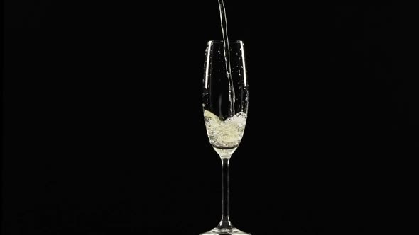 Sparkling Yellow Water is Pouring Into Wineglass Standing on Black Background in Slowmotion