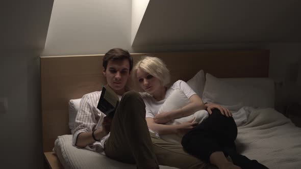 Young Couple in Love Lying in the Bed and Reading Book