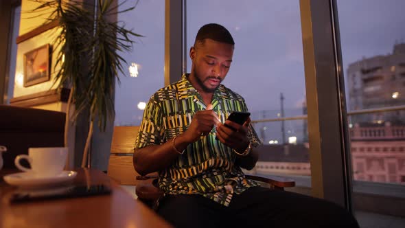 AfricanAmerican Man Looking in Smartphone and Drink Coffee