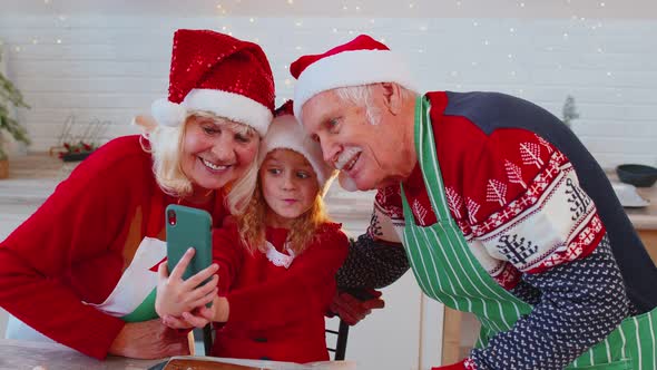 Senior Grandparents with Granddaughter Kid Taking Selfie Photo on Mobile Phone at Christmas Kitchen