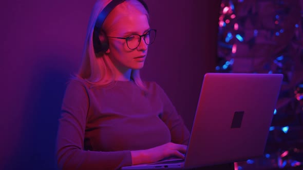 Female Working with Headphones a Tablet and a Laptop on a Colorful Neon Light Background