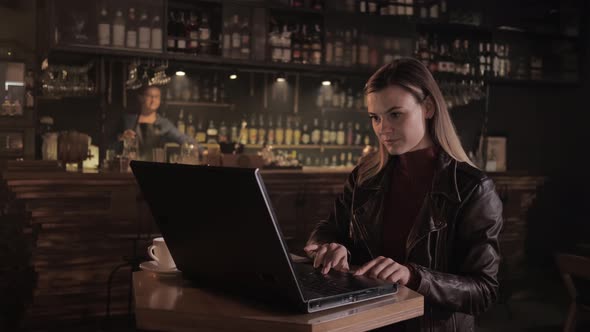 Successful Female Entrepreneur Working at Computer While Sitting at Table in Trendy Bar Folds Her