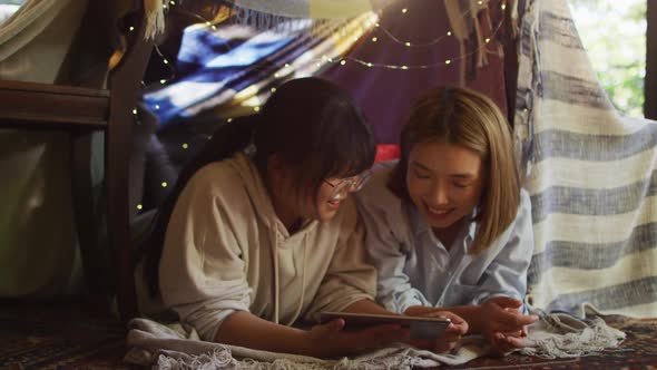 Asian mother and daughter smiling while using digital tablet under blanket fort at home