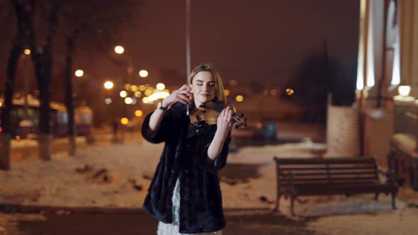A Beautiful Girl is Playing the Violin in the Centre of the City in the Winter