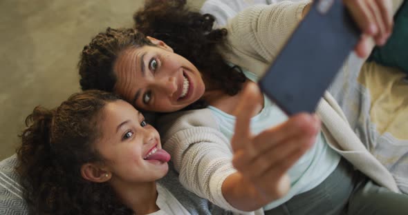 Happy mixed race mother and daughter laying on the floor,having fun and taking selfie