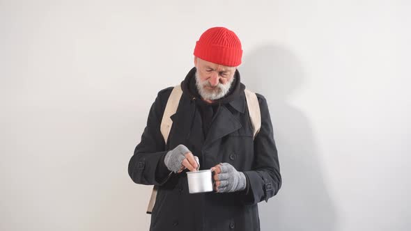 Portrait of a Homeless Beggar in Studio on White Background Pulls Bills Out of Cup for Money