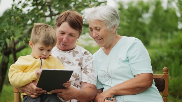 Grandmothers Look at a Tablet in the Hands of a Grandson