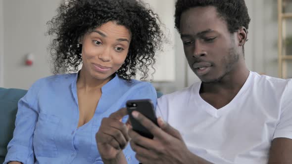 African Couple Reacting To Online Loss on Smartphone