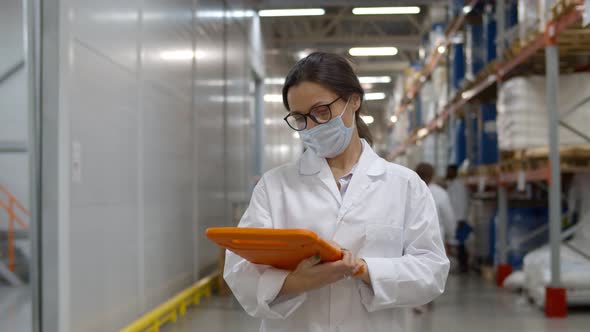 Supervisor in Uniform and Mask Using Tablet for Checking Data While Standing in Warehouse