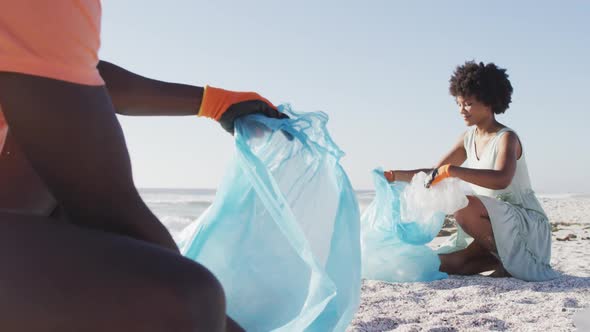 African american couple segregating waste with gloves on sunny beach