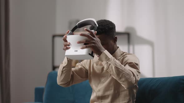 Young Black Man is Putting Headmounted Display on Head Sitting Alone in Room Virtual Reality Resting