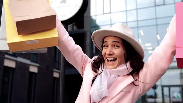 Happy Girl Hides and Looks Out of the Multicolored Shopping Bags in the Street