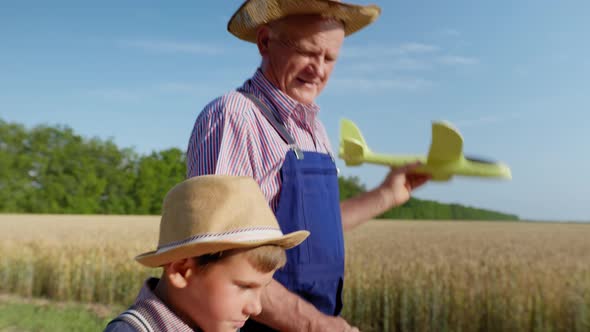 Boy Playing with Toy Airplanes Along with Elderly Grandfather in Straw Hats Backdrop of Field
