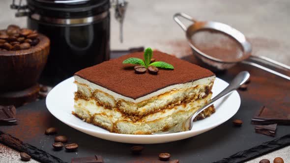 Portion of Traditional Italian Tiramisu dessert and hand coffee grinder on grey concrete background