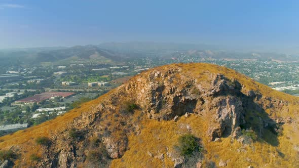 Aerial View of the American Flag Waving on the Top of the Rocky Hill with Cityscape on Background alt