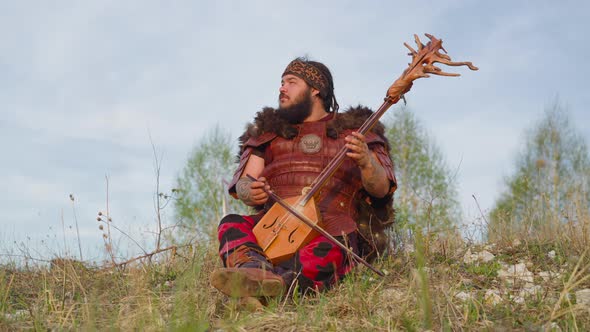 Dreaming Man Plays Stringed Instrument Sitting on Hill Grass