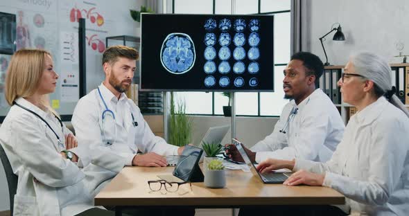 Male and Female Doctors Sitting Around Meeting Table in Medical Room and Discussing