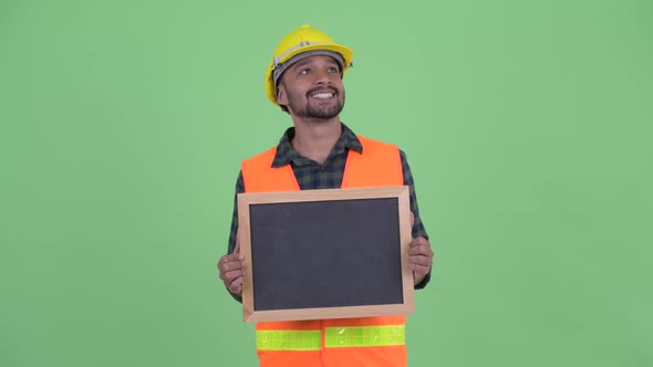 Happy Young Bearded Persian Man Construction Worker Thinking While Holding Blackboard