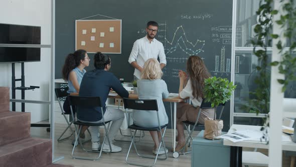 Zoomin of Successful Business Team Discussing Sales Development and Clapping Hands in Office