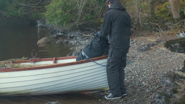 Young man takes backpack from bow of lake boat MID SHOT