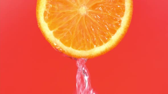 Water falling from orange hue orange on red background. Orange slice and water splashing, drops