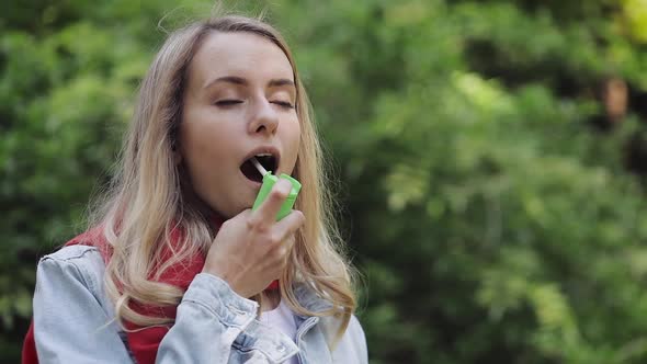 Young Woman Using Throat Spray Standing on the Park Background. Health and Medical Concept.