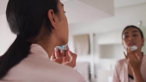 Mixed race gender fluid person standing in bathroom and putting shaving cream on