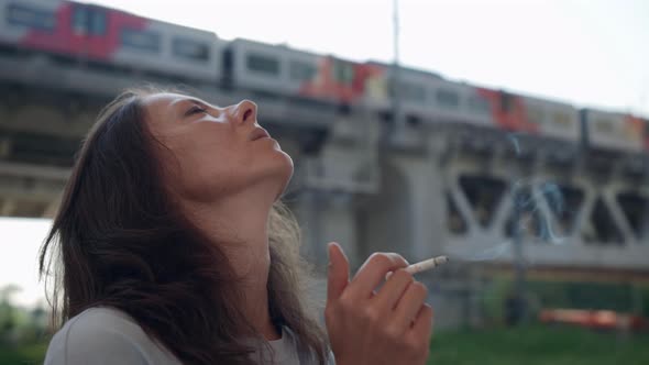 Adult Woman is Smoking Cigarettes Standing Under Railway Bridge in City Outskirts Portrait