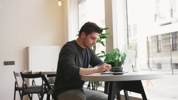 Young Hipster Businessman Working on Laptop in Cafe and Drinking Coffee