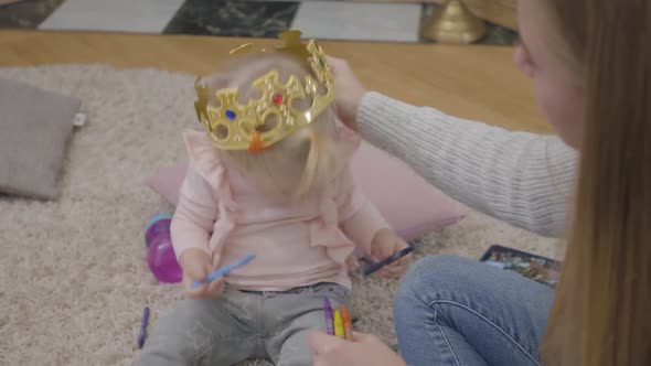 Close-up of Young Caucasian Mother Trying To Put Toy Crown on Daughter's Head