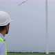 Engineer with beard puts on white helmet, looks at wind turbine generating electricity. - VideoHive Item for Sale