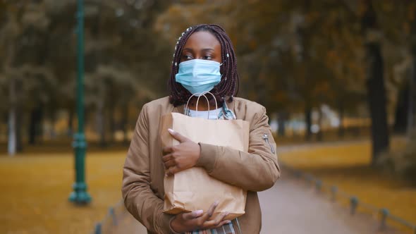 African Woman Carrying Shopping Bag with Groceries While Wearing Mask Outdoors